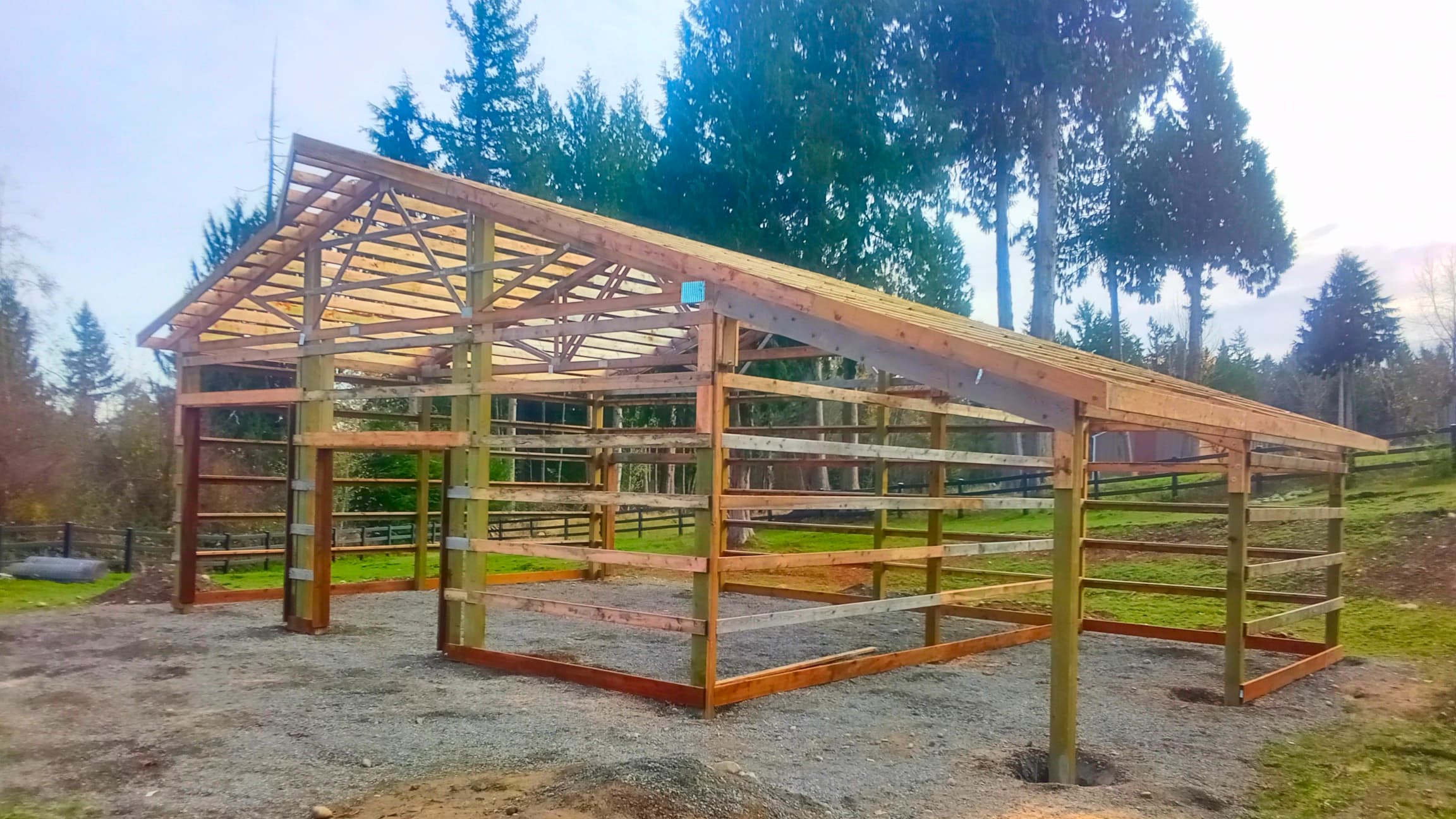 Side view of a 14' tall post-frame structure showing the detailed craftsmanship of this 36'x36' pole building under construction by Probuilt Metal Buildings. The durable pressure-treated posts and engineered trusses form the backbone of this custom metal building in Lake Tapps, designed to withstand Pacific Northwest weather conditions.