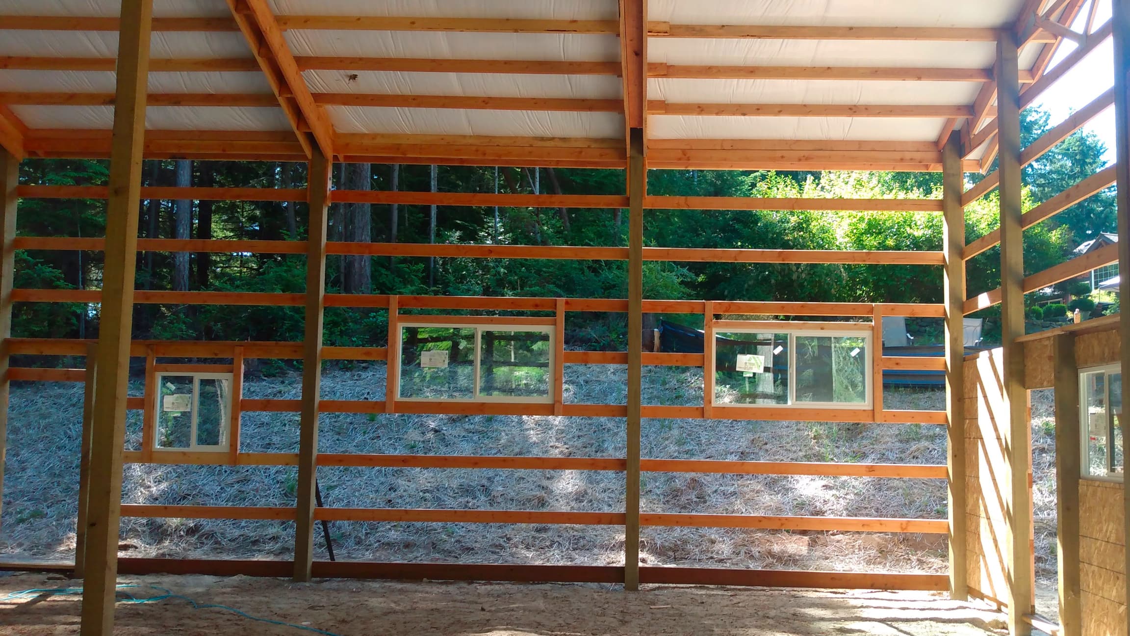 Inside view of a 36'x36' post-frame building by Probuilt Metal Buildings in Olalla showing completed wall framing and window placements. This 16' tall structure features an open-concept design with strategic window placement for natural lighting.